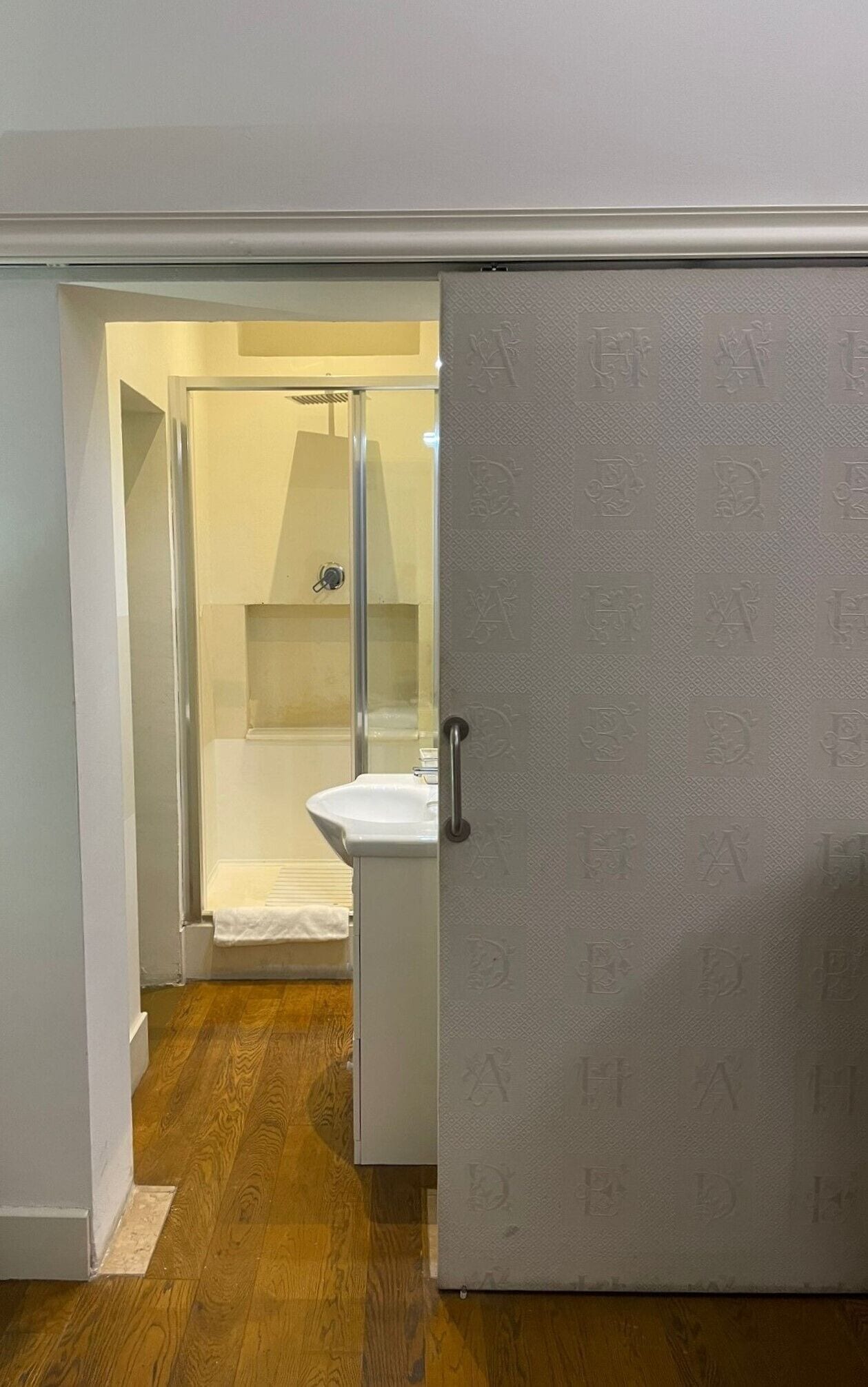Un baño con cabina de ducha de vidrio, un lavabo blanco y una toalla colgada en la pared.