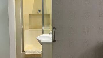 Un baño con cabina de ducha de vidrio, un lavabo blanco y una toalla colgada en la pared.