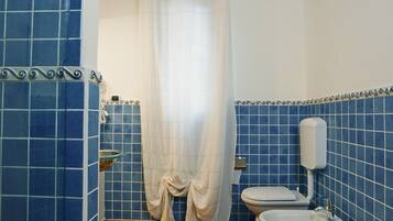A bathroom with blue tiles, a wooden floor, a toilet, a bidet, and a shower curtain.