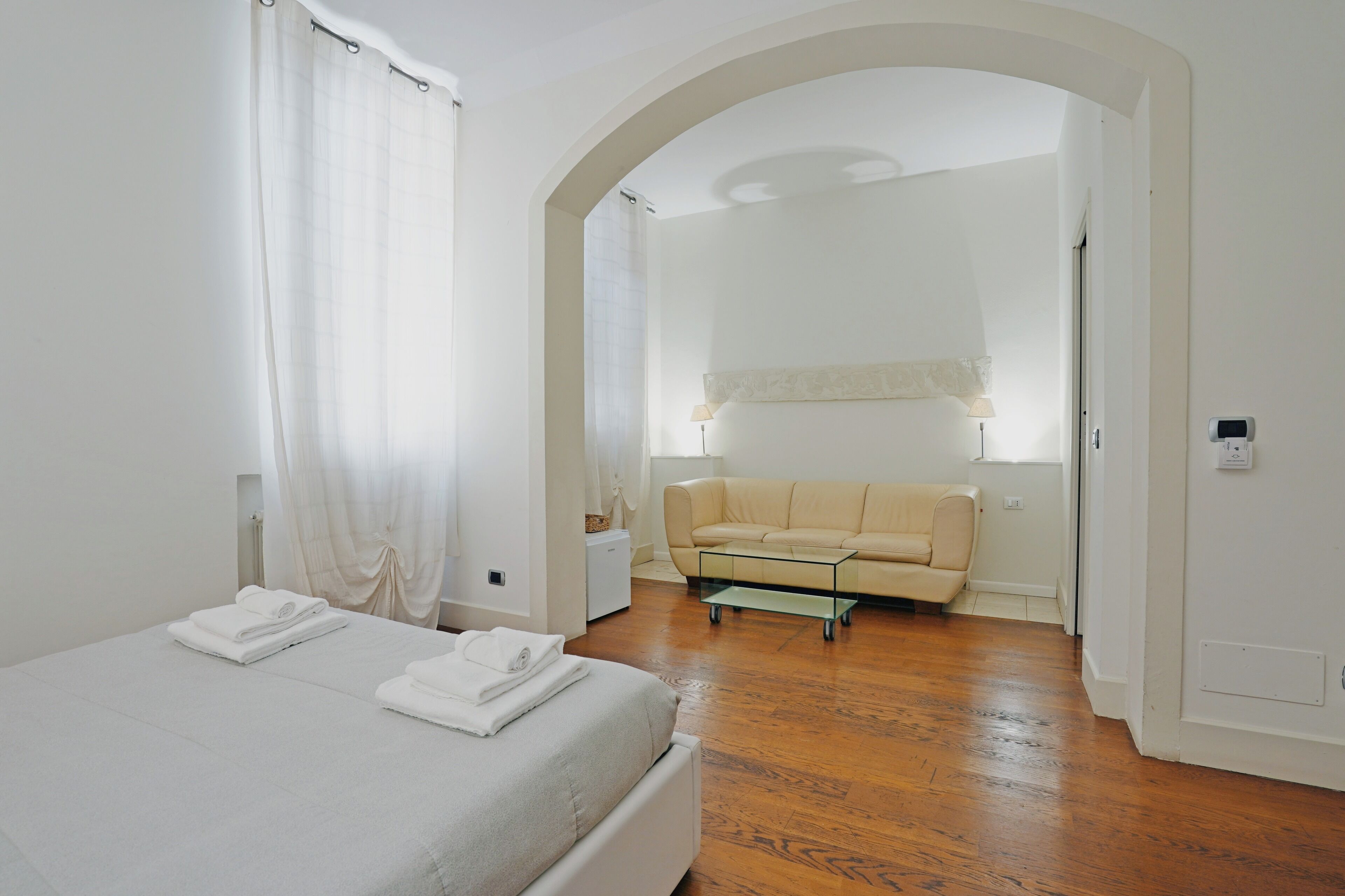 Un dormitorio con cama, sofá, una mesita y una ventana con cortinas.