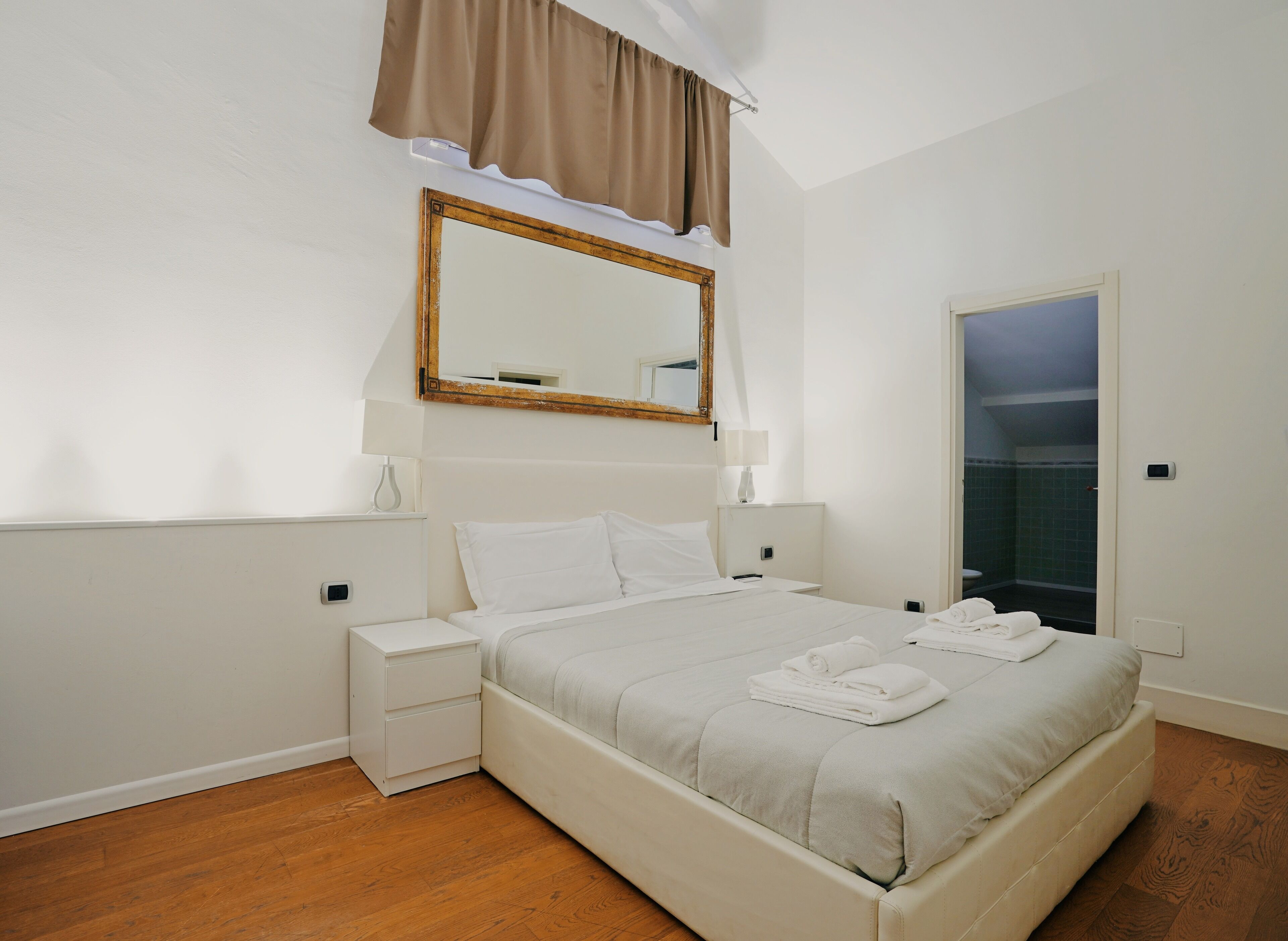Une chambre à coucher bien rangée, avec un lit, des tables de chevet, un miroir et une porte donnant sur une salle de bain.