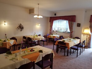 A dining area with multiple tables set for meals, chairs, and a chandelier. - Landhotel Trampe (Breydin)