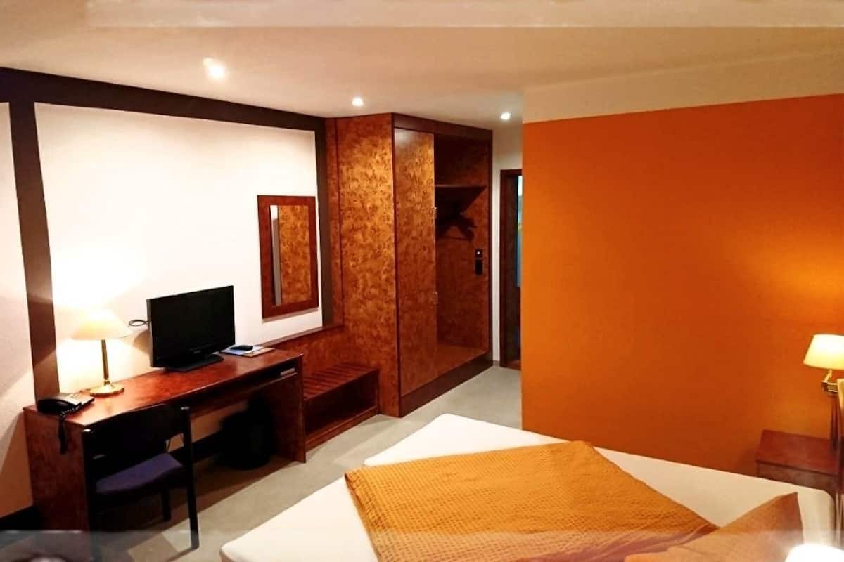 A hotel room with a bed, desk, chair, and a wardrobe.