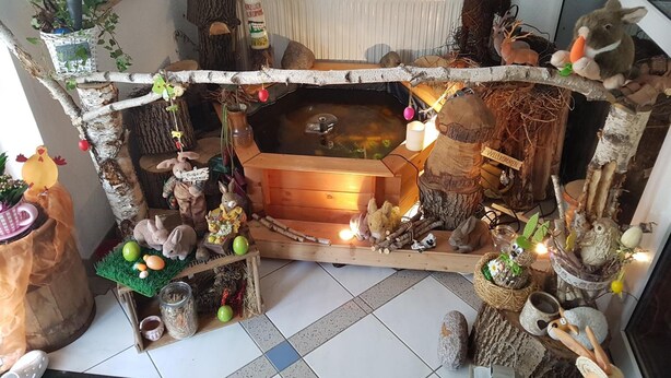 A cozy indoor setting with a wooden bench, a small pond, and various decorative items like stuffed animals and plants. - Landhotel Trampe (Breydin)