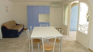 A dining area with a white table and chairs, a blue cabinet, and a patterned sofa. - Flat in Lignano Riviera (Lignano Sabbiadoro)