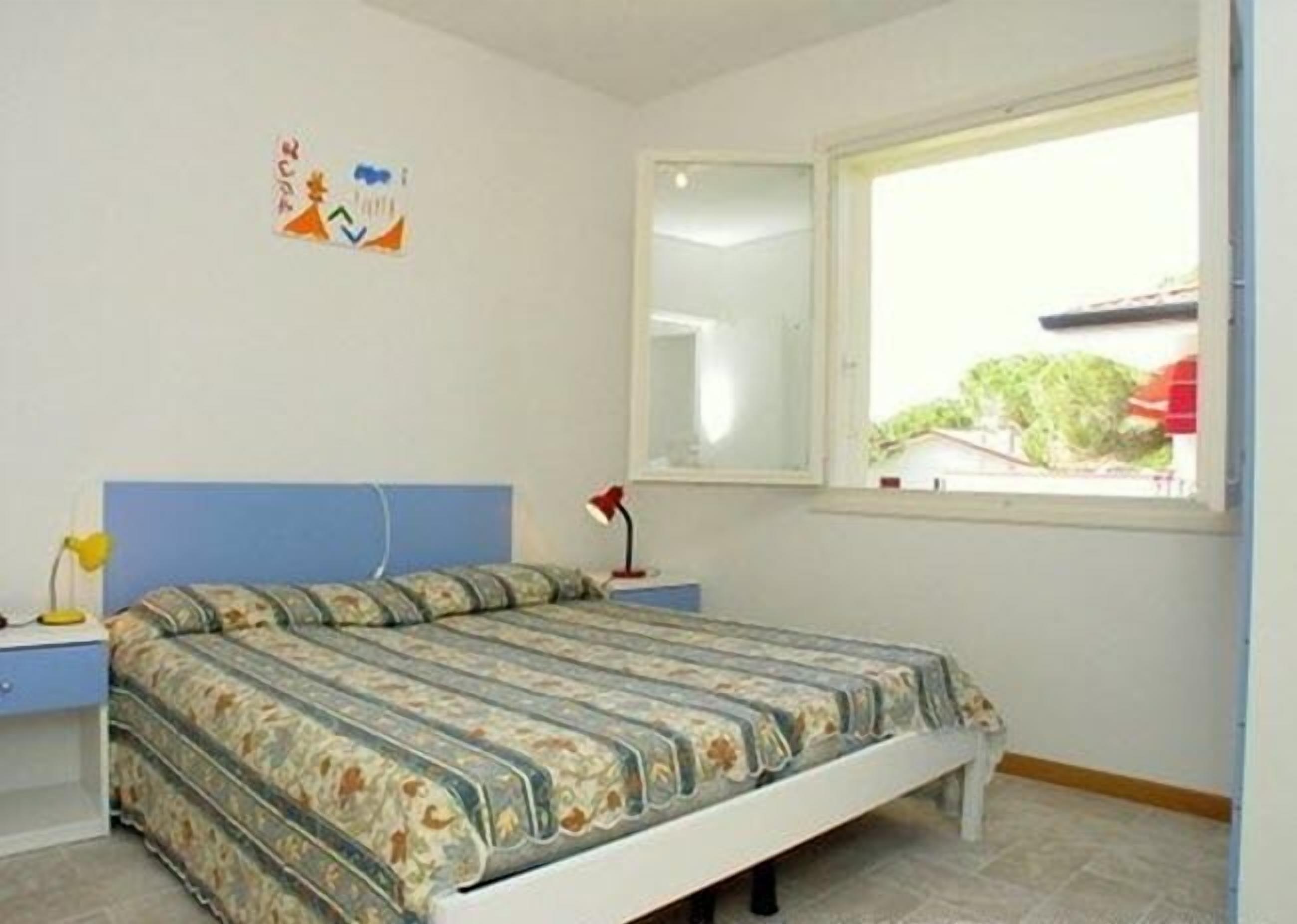 A bedroom with a bed, a nightstand, a lamp, a window with a view, and a wall decoration.