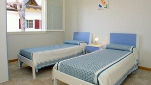 A room with two single beds, a window with a view of a house, and a wall-mounted light switch. - Flat in Lignano Riviera (Lignano Sabbiadoro)