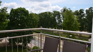 Ein Balkon mit Korbstühlen, einem Metallgeländer und Blick auf eine Straße und Bäume.
