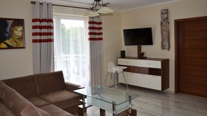 Ein modernes Wohnzimmer mit einem Glastisch, einem braunen Sofa, einem weißen Hochstuhl, einem Holzschrank und einem an der Wand befestigten Flachbildfernseher.