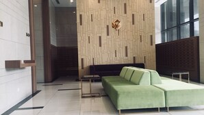 Um hall moderno com um sofá modular verde, uma mesa de centro de vidro e uma parede com padrão geométrico.