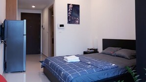 Quarto moderno com cama, mesa de cabeceira pequena, ar condicionado fixado na parede e porta que dá para outro cômodo.