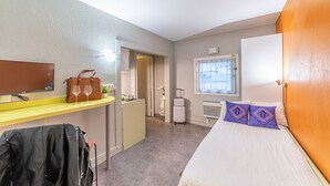 Ein Hotelzimmer mit einem Bett, einem Schreibtisch, einem Laptop, einem Koffer und einem Fernseher.