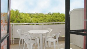 A balcony with a round table and four white chairs, overlooking a green landscape with buildings in the distance.