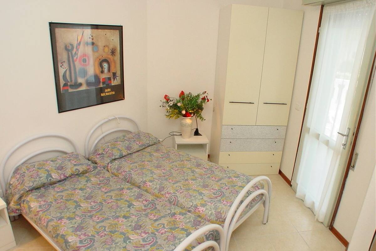 A bedroom with a double bed, a bedside table with a lamp, a wardrobe, and a framed picture on the wall.