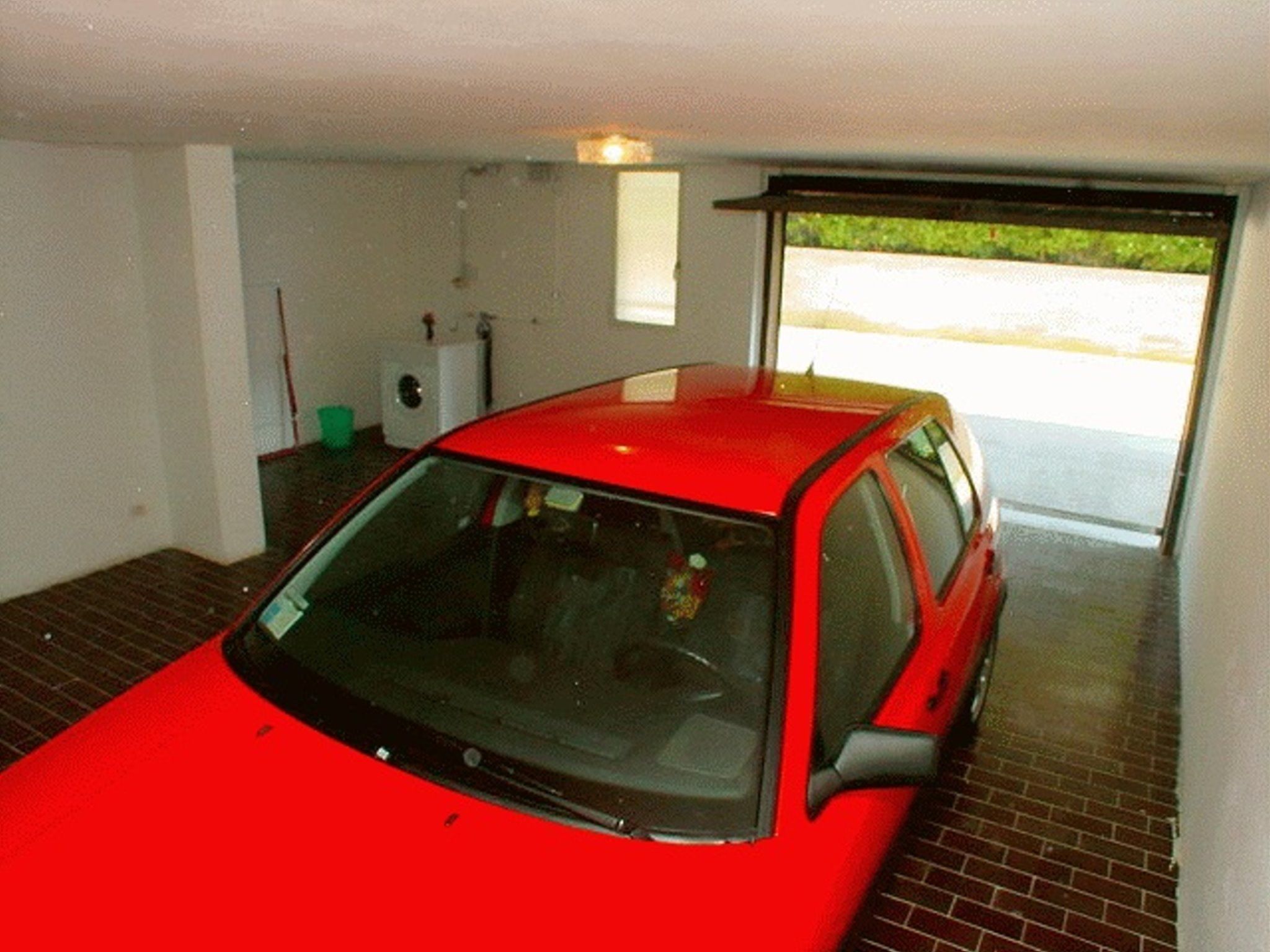 En röd bil står parkerad i ett garage med ett tegelgolv och en vit vägg.