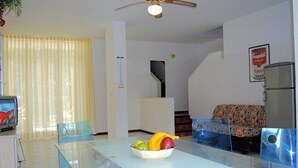 A compact living space with a dining area, a sofa, a ceiling fan, and a refrigerator. - Villa a Lignano Pineta (Lignano Sabbiadoro)