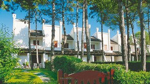 A row of white buildings with multiple chimneys, surrounded by trees and greenery. - Villa a Lignano Pineta (Lignano Sabbiadoro)