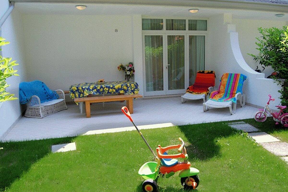 A patio with a lawnmower, a bench, and two chairs.