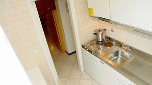 A kitchen with a stainless steel sink, a stove, and a white cabinet. - Villa a Lignano Pineta (Lignano Sabbiadoro)