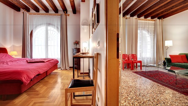 Ein Hotelzimmer mit Holzboden, einem Bett, einem Schreibtisch, einem Sessel und einem roten Teppich.