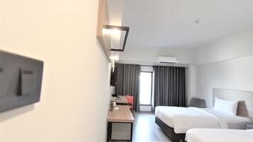 Habitación de hotel con dos camas, un escritorio, una silla, un televisor y un aire acondicionado.