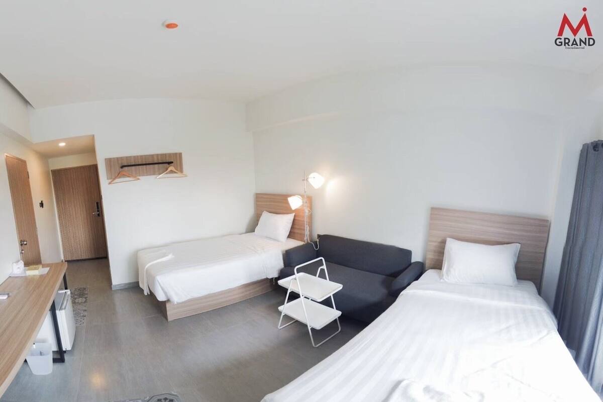 Habitación de hotel con dos camas, un escritorio, una silla y un perchero.