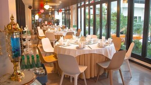 A restaurant with round tables, white chairs, and a view of greenery outside.