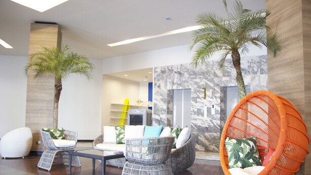 A modern lobby with wicker furniture, a glass coffee table, and a large orange chair.