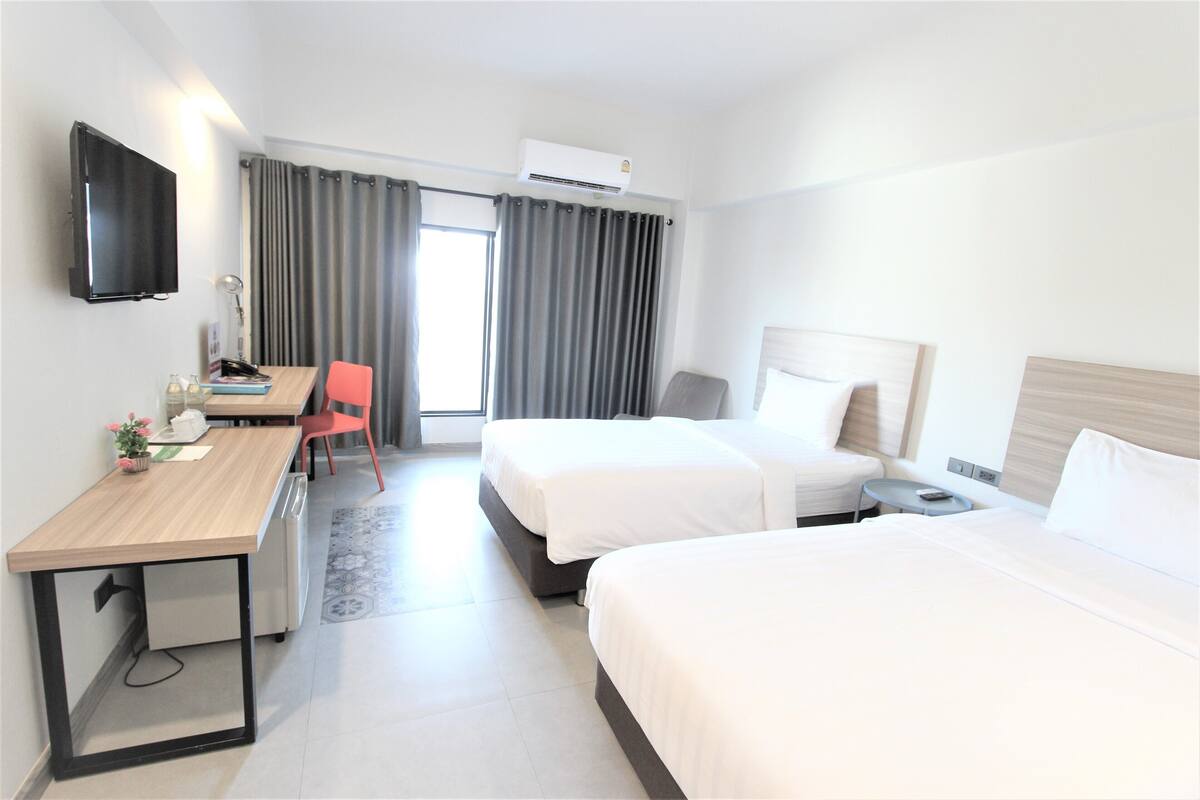 Una habitación de hotel con dos camas, un escritorio con silla, un televisor y un equipo de aire acondicionado.