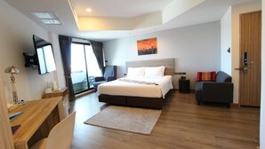 A modern hotel room with a large bed, a desk, a chair, a sofa, a TV, and a window with curtains.