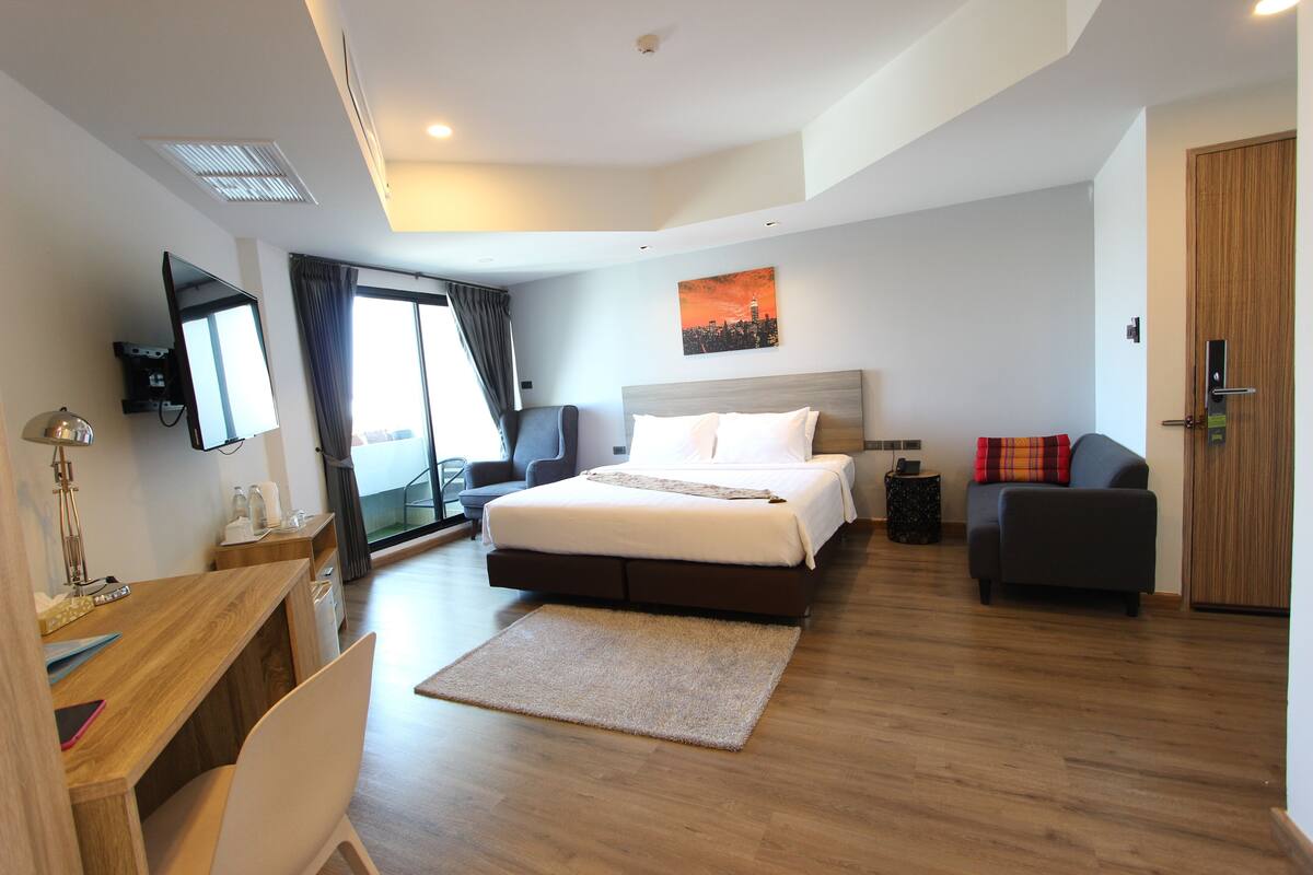 Una habitación de hotel moderna con una cama grande, un escritorio, una silla, un sofá, un televisor y una ventana con cortinas.