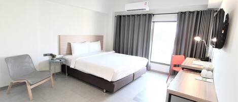 Habitación de hotel con cama, escritorio, silla, televisión y ventana con cortinas.