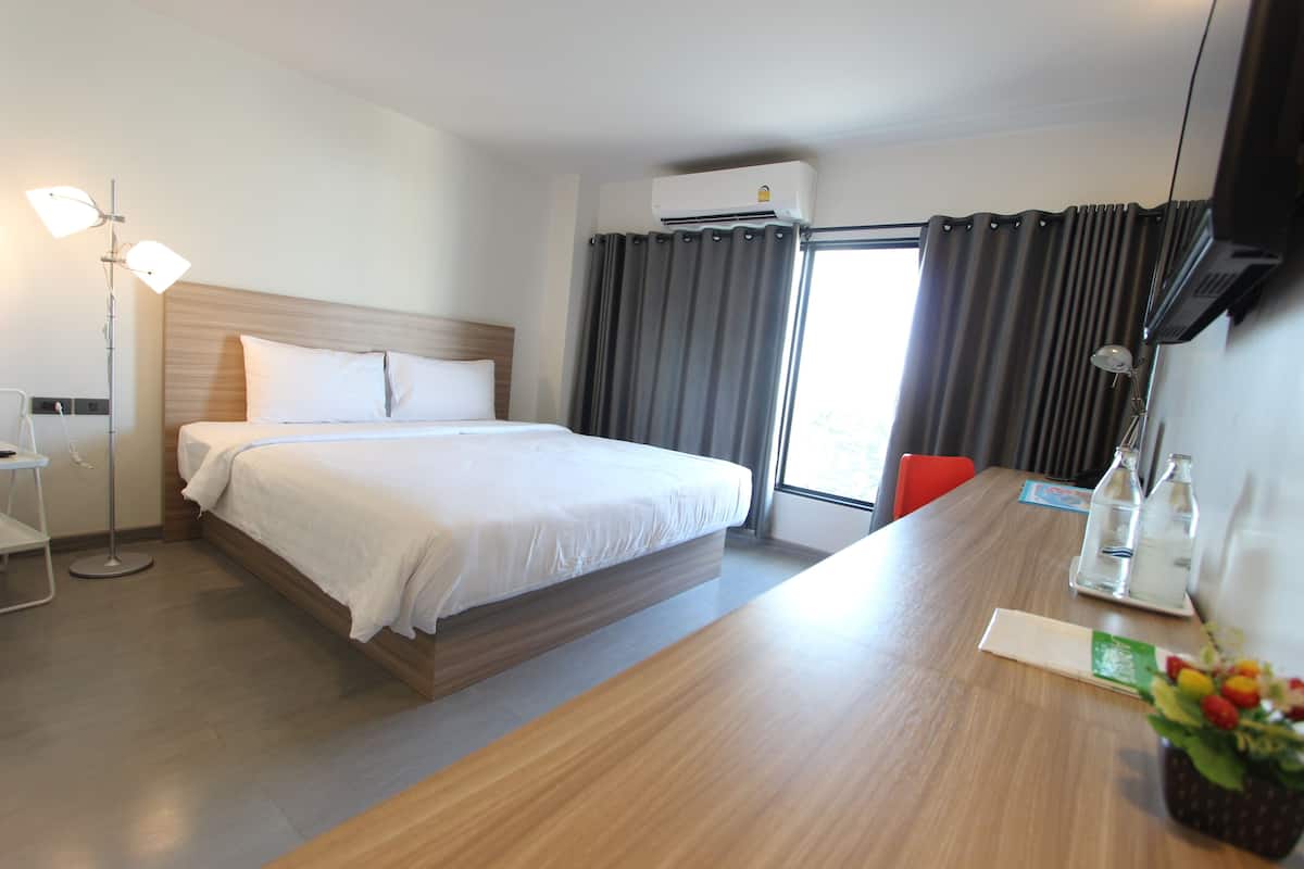 Habitación de hotel con cama, mesita de noche, lámpara y ventana con cortinas.