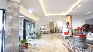 A modern hotel lobby with marble columns, a patterned rug, and wicker furniture.