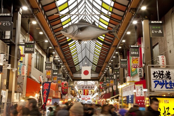 Un mercado interior concurrido, con un pescado grande colgando del techo, varios puestos de comida y letreros en un idioma extranjero.