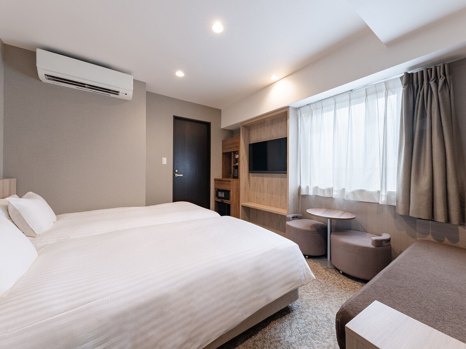 Una habitación de hotel moderna con una cama grande, un televisor, una mesita pequeña y una zona de estar.