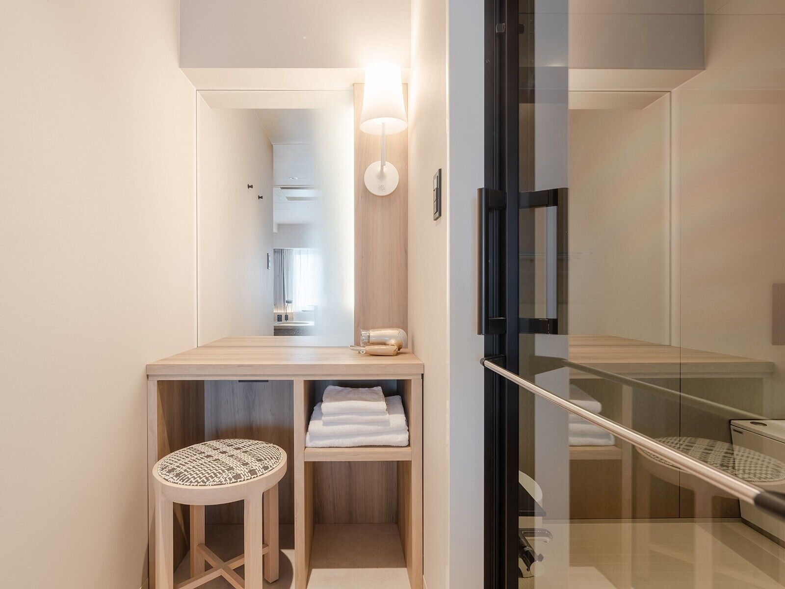 A modern bathroom with a wooden vanity, a round stool, and a glass shower enclosure.
