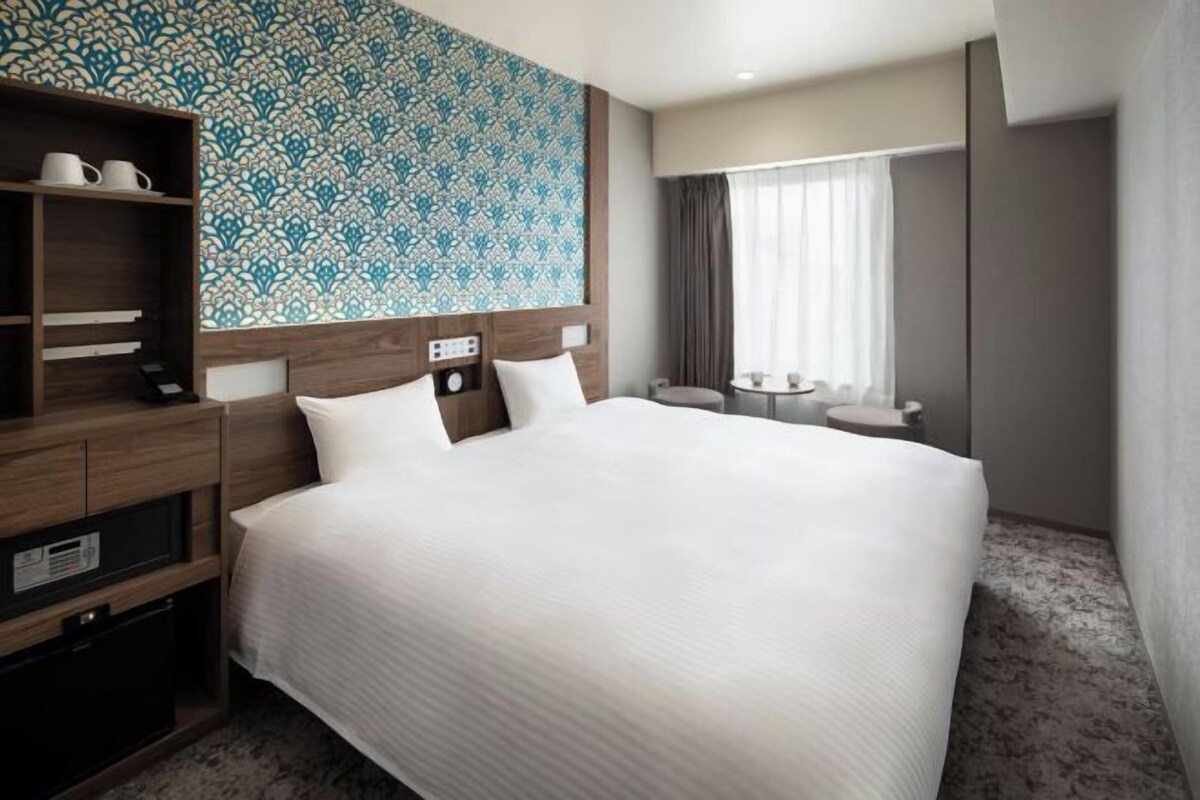 A hotel room with a large bed, a wooden headboard, a small bedside table, a radio, and a patterned wall.