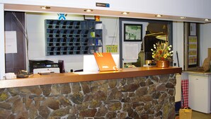 A reception desk with a stone wall, a blue sign with an 'X', and a flower arrangement. - Hotel Panda (Pas de la Casa)
