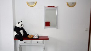 A room with a white wall, a red vanity table, a panda plush toy, a mirror, and two wall sconces. - Hotel Panda (Pas de la Casa)