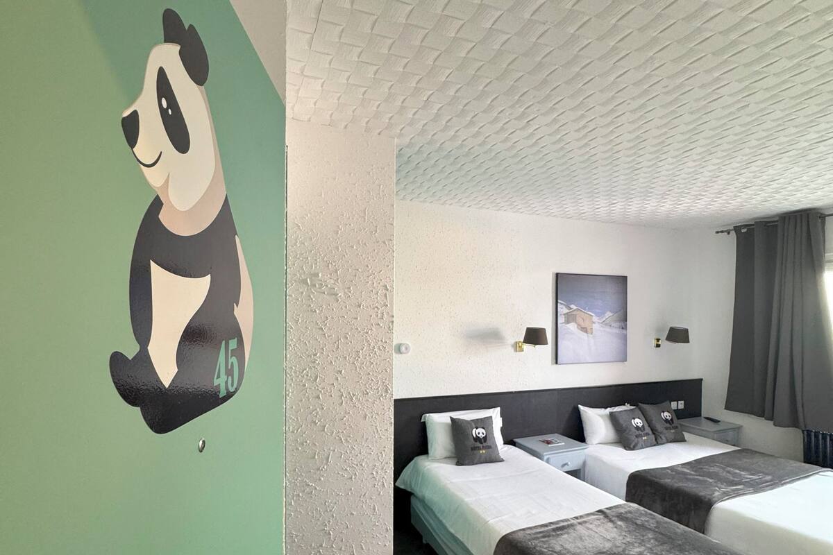 Une chambre d’hôtel avec deux lits, un mur d’accent vert, une décoration sur le thème des pandas et un plafond texturé.