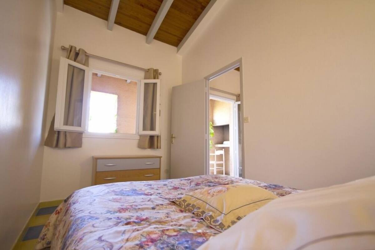Um quarto com cama, janela com cortinas, mesa de cabeceira e guarda-roupa.