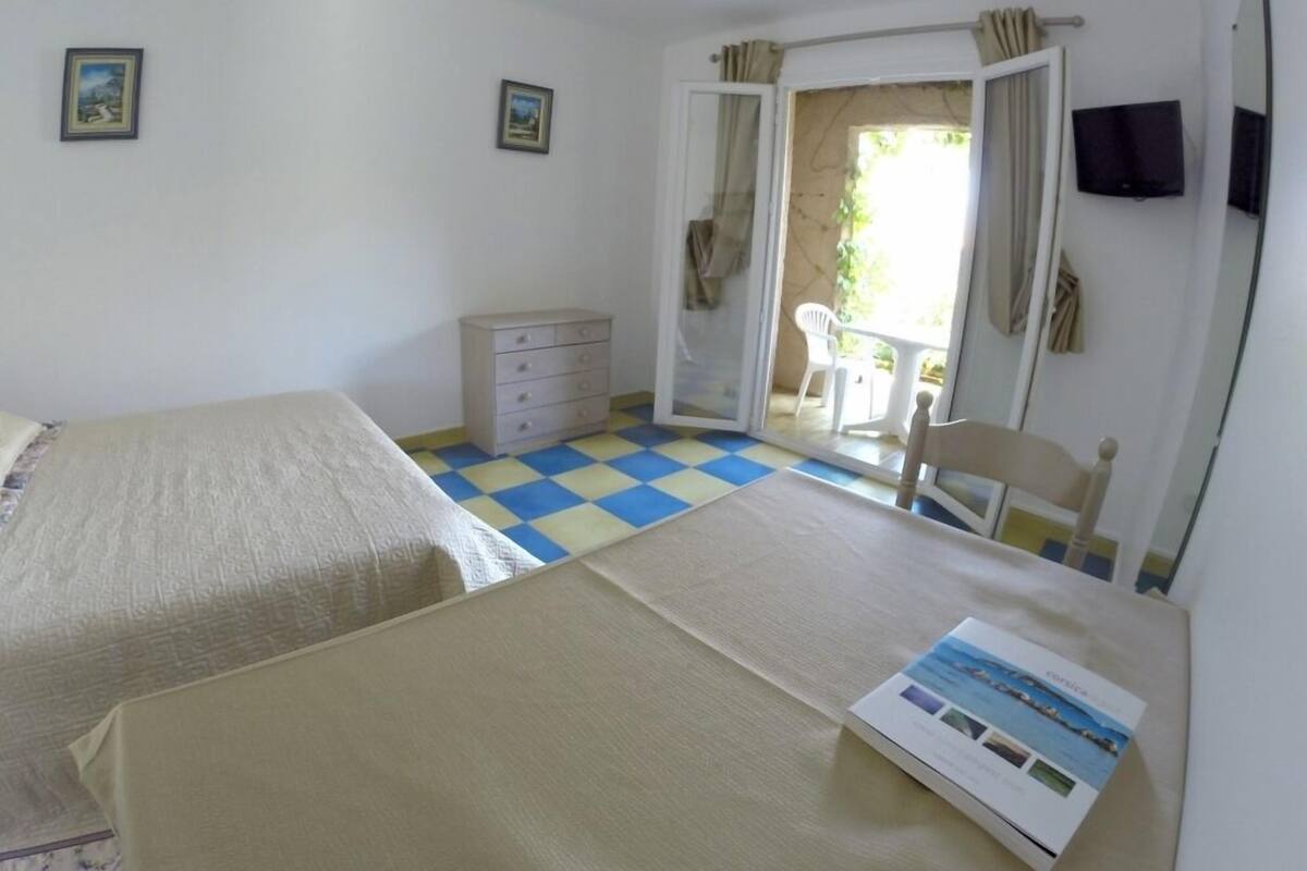 Um quarto com piso quadriculado, uma cama, cômoda, cadeira e televisão na parede.