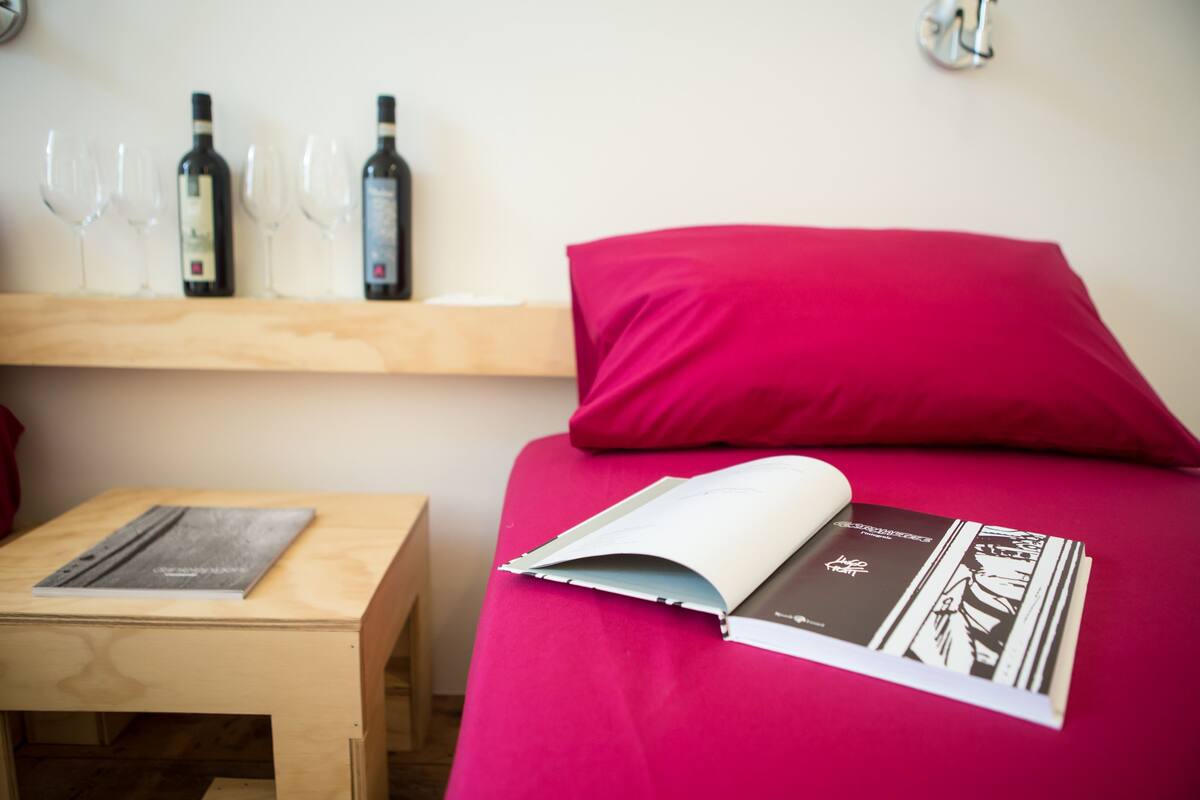 Una habitación con una cama, una mesa de madera y una estantería con botellas de vino y copas.