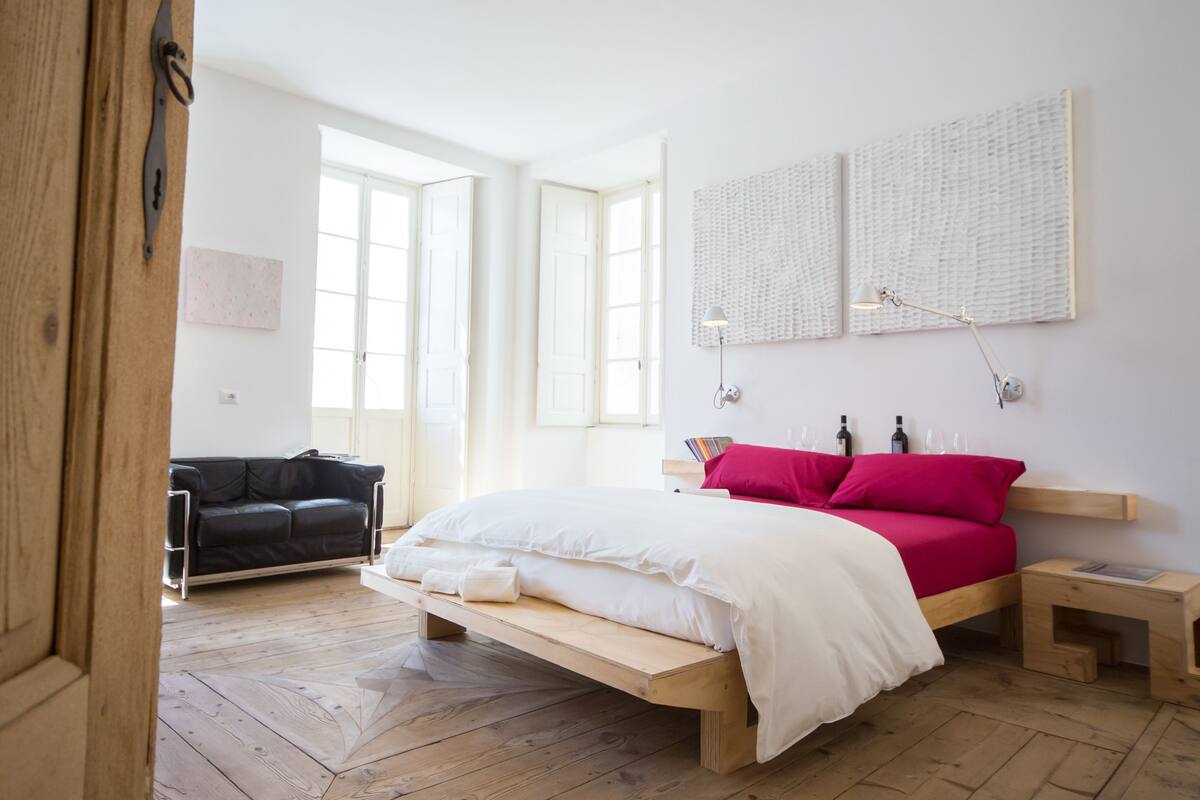 Un dormitorio con una cama de madera, un sofá de cuero negro y dos ventanas grandes.