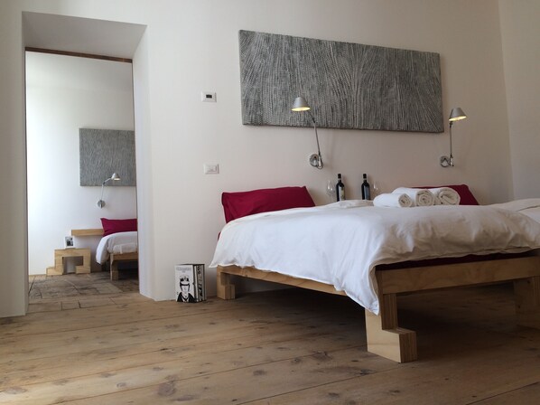Une chambre à coucher avec un lit en bois, une literie blanche, des coussins rouges, deux lampes de chevet et une grande œuvre d’art texturée accrochée au mur.