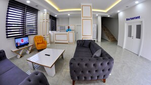 En moderne hotellobby med reception, sofaer, et fjernsyn og en trappe til restauranten.