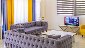 En moderne stue med en stor, betrukken sofa, et sofabord og et fjernsyn på et stativ.