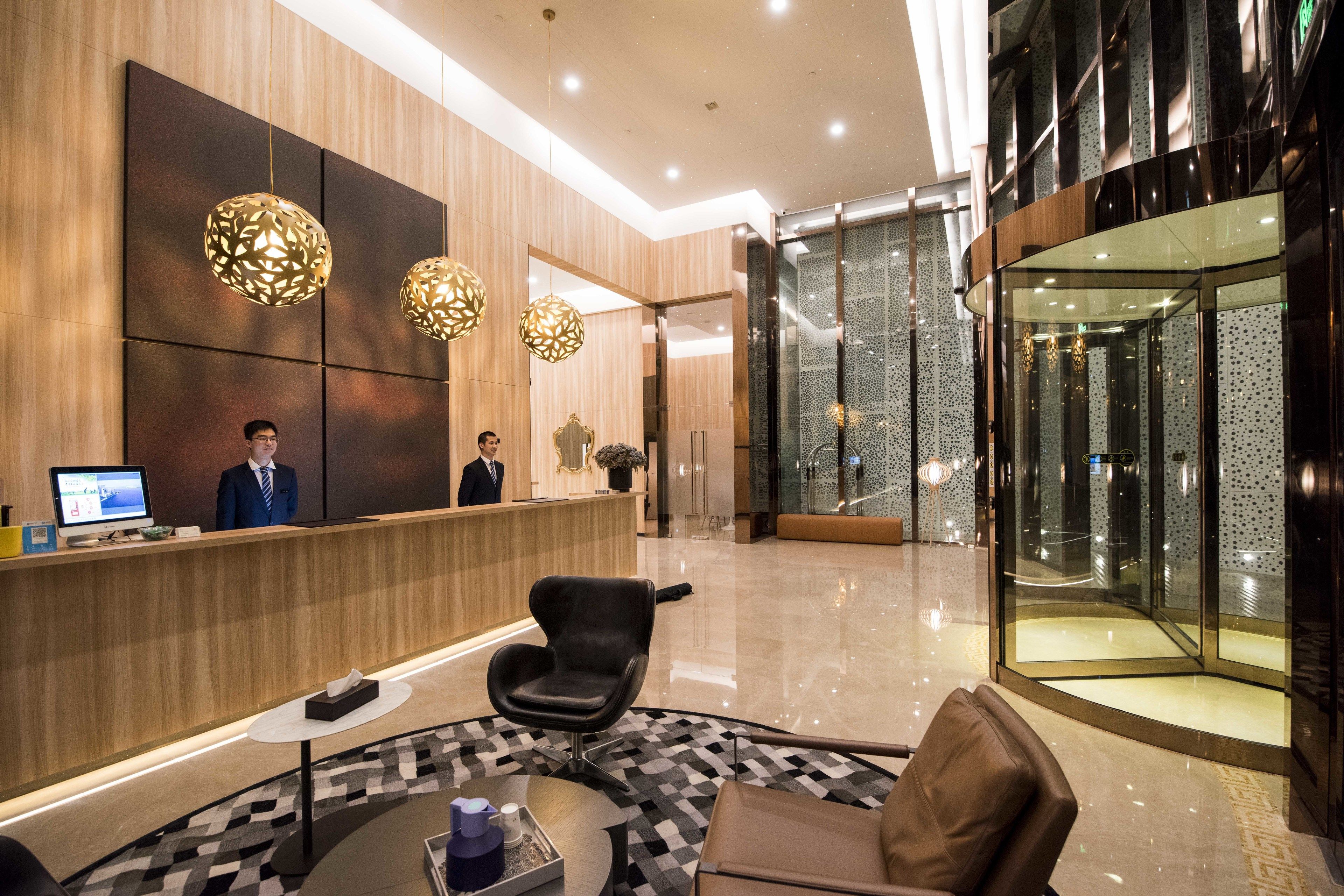 Un hall d’hôtel moderne avec un comptoir d’accueil, un espace salon et un ascenseur en verre.