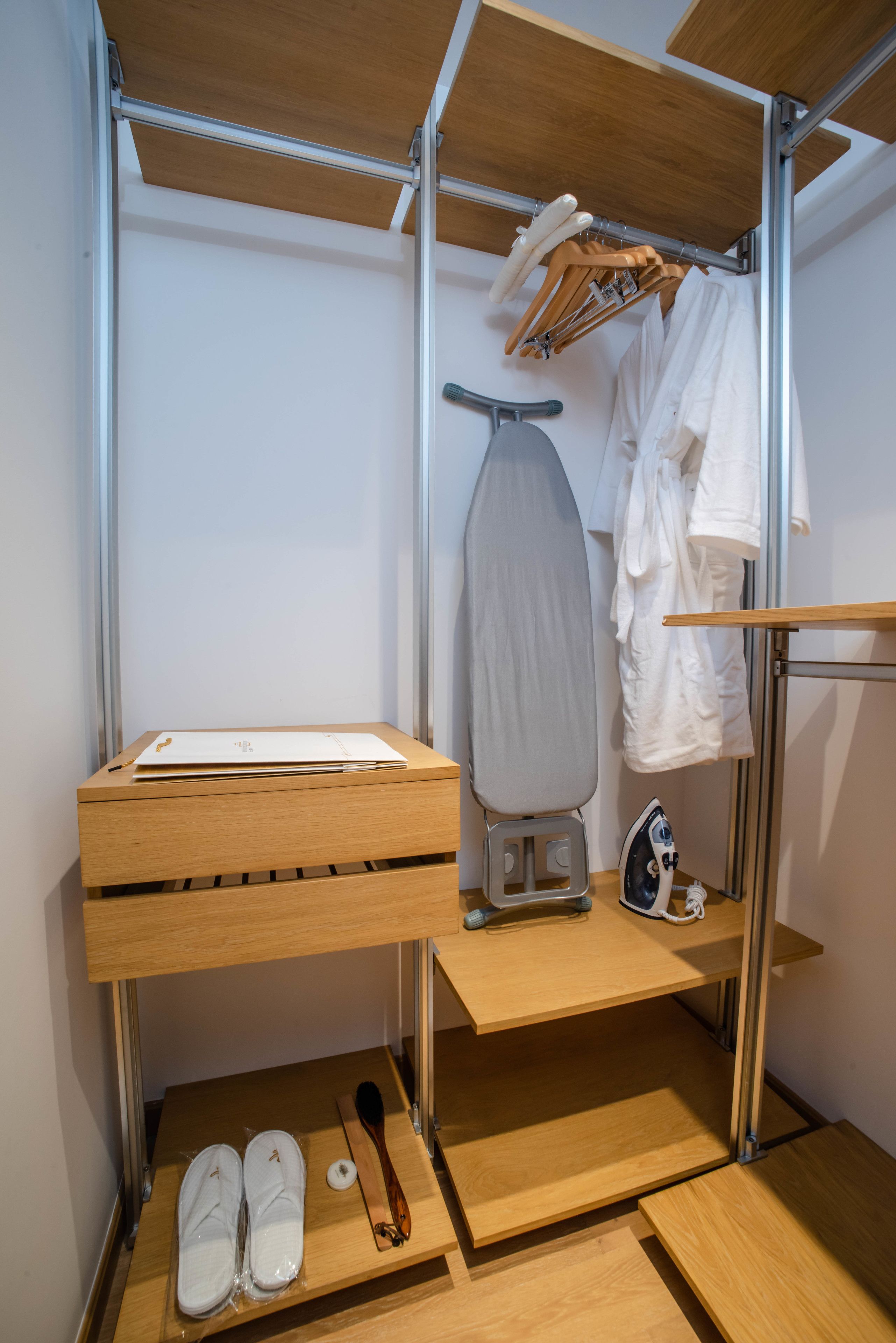 Casa de banho compacta e moderna com toucador de madeira, espaço para passar roupa integrado e um cabideiro para roupões.